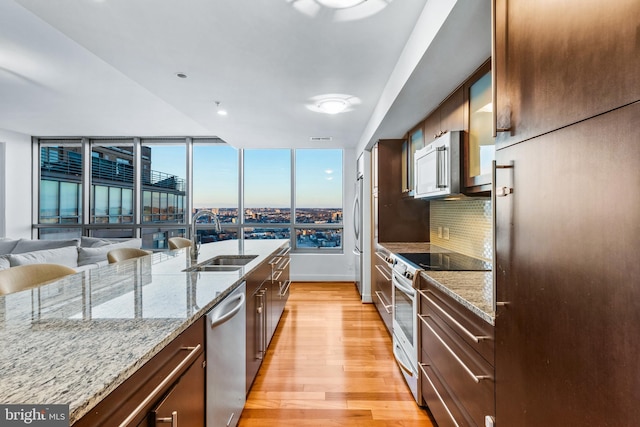 kitchen with tasteful backsplash, sink, light hardwood / wood-style flooring, appliances with stainless steel finishes, and light stone counters