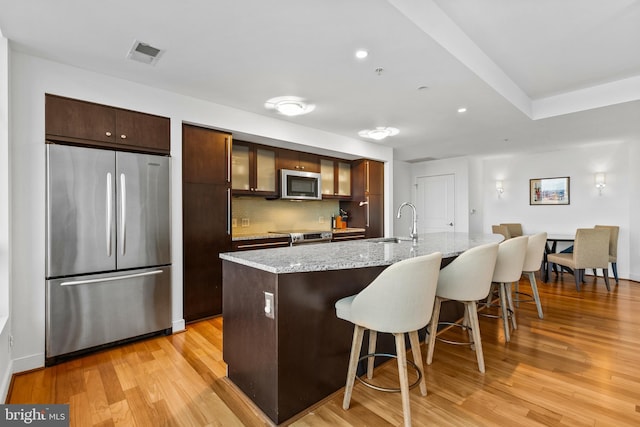 kitchen with sink, light wood-type flooring, a kitchen breakfast bar, an island with sink, and stainless steel appliances