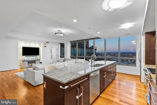 kitchen featuring dark brown cabinetry, a fireplace, an island with sink, sink, and light wood-type flooring