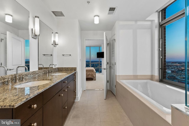 bathroom with a relaxing tiled tub, vanity, and tile patterned flooring