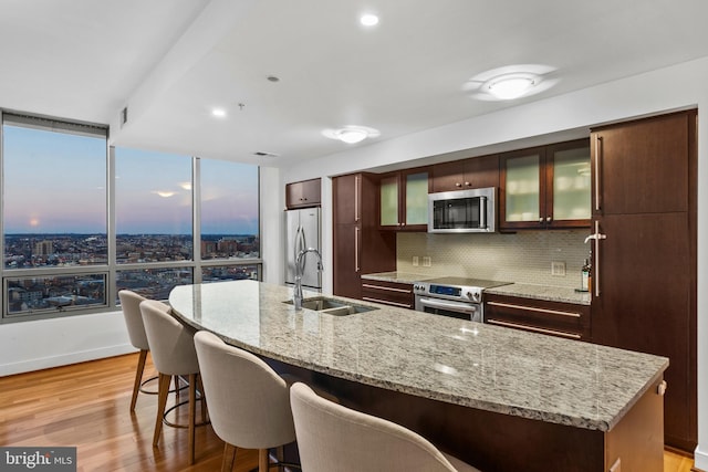 kitchen featuring a center island with sink, decorative backsplash, sink, light hardwood / wood-style flooring, and appliances with stainless steel finishes