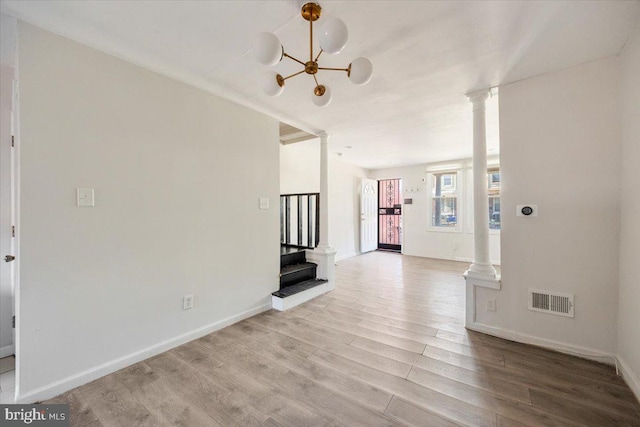 unfurnished living room with an inviting chandelier, ornate columns, and light hardwood / wood-style floors