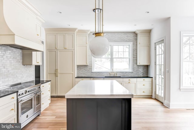 kitchen featuring double oven range, backsplash, custom range hood, and decorative light fixtures