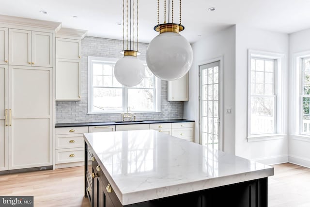 kitchen with pendant lighting, a kitchen island, dark stone countertops, decorative backsplash, and sink