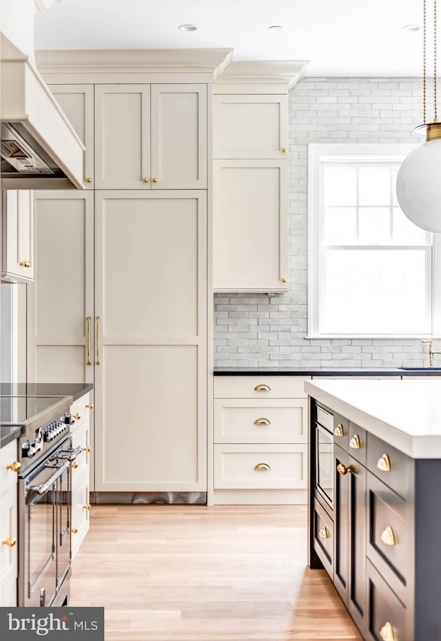 kitchen featuring premium range hood, light hardwood / wood-style floors, high end stove, decorative backsplash, and hanging light fixtures