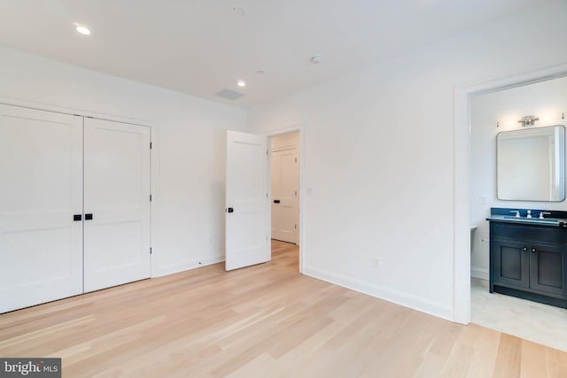 unfurnished bedroom with a closet, ensuite bathroom, light hardwood / wood-style flooring, and sink