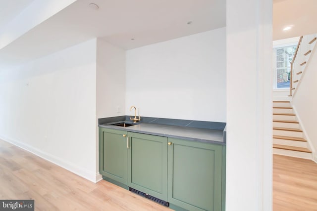 bar featuring sink, green cabinetry, and light hardwood / wood-style floors