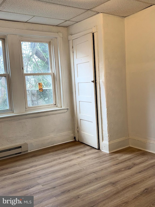 empty room with a drop ceiling, a baseboard heating unit, and hardwood / wood-style floors