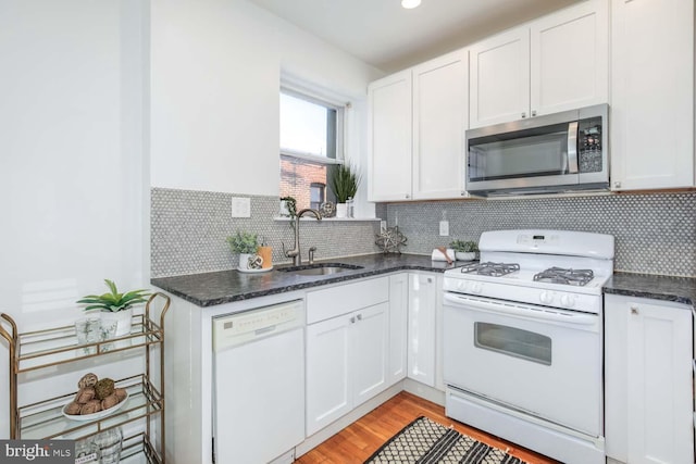 kitchen featuring sink, white cabinetry, white appliances, dark stone counters, and decorative backsplash