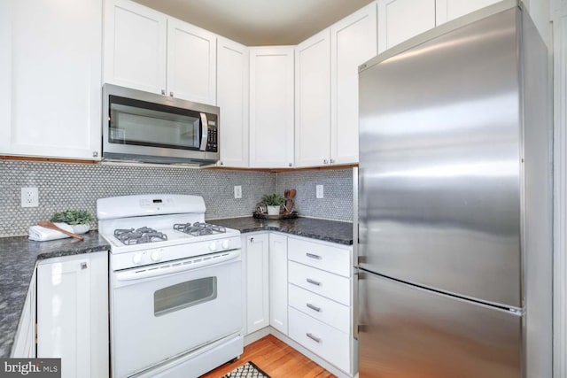 kitchen with backsplash, stainless steel appliances, dark stone counters, and white cabinets