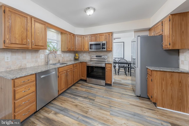 kitchen featuring light stone countertops, appliances with stainless steel finishes, sink, and light hardwood / wood-style flooring