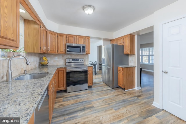 kitchen featuring tasteful backsplash, sink, light wood-type flooring, appliances with stainless steel finishes, and light stone counters