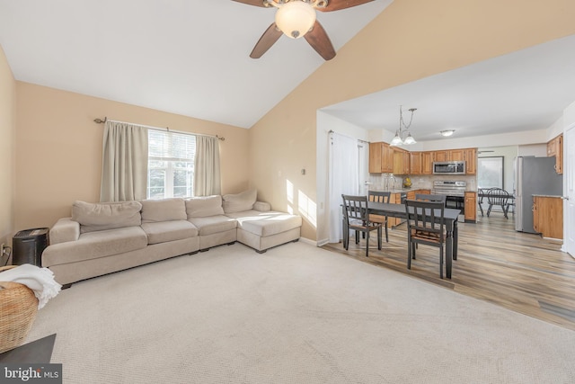 living room with ceiling fan with notable chandelier, light wood-type flooring, and vaulted ceiling