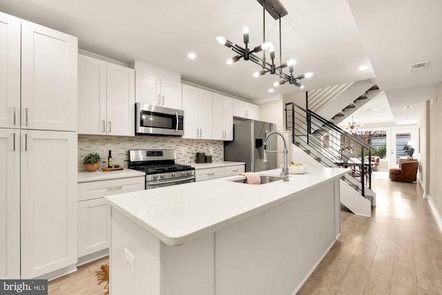 kitchen with appliances with stainless steel finishes, white cabinets, sink, decorative light fixtures, and an island with sink