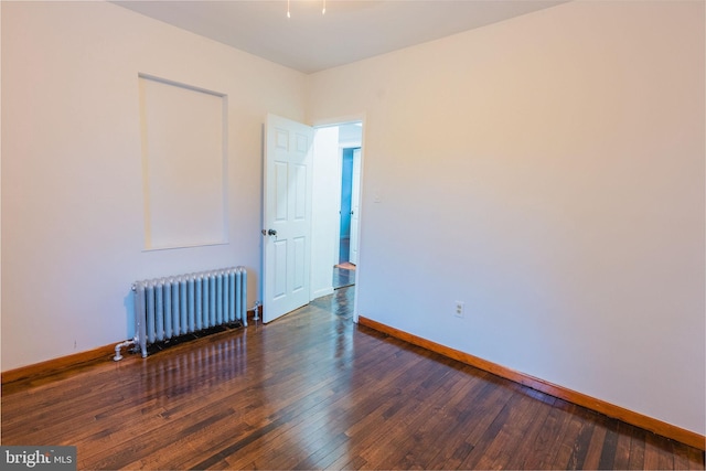 unfurnished room featuring radiator heating unit and dark hardwood / wood-style floors