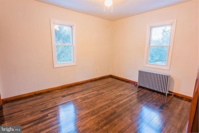 spare room with a wealth of natural light, dark wood-type flooring, and radiator heating unit