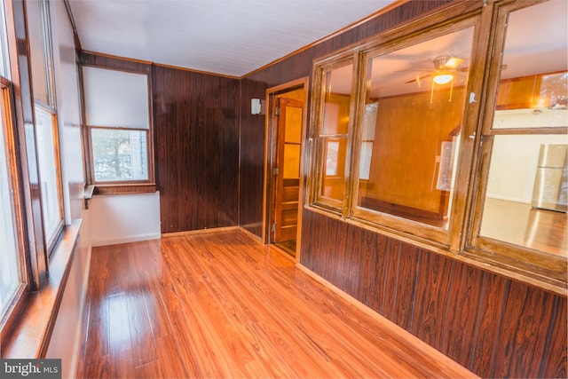 unfurnished room with hardwood / wood-style flooring, ceiling fan, ornamental molding, and wood walls