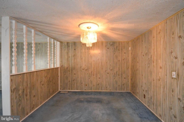 spare room with a notable chandelier, wood walls, a textured ceiling, and dark colored carpet