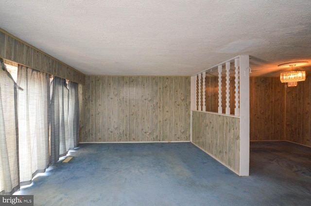 spare room with wood walls, a chandelier, a textured ceiling, and dark colored carpet