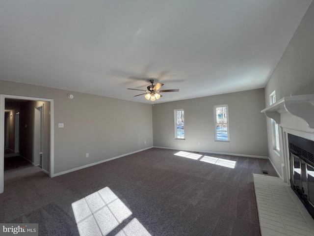 unfurnished living room with ceiling fan, dark carpet, and a fireplace