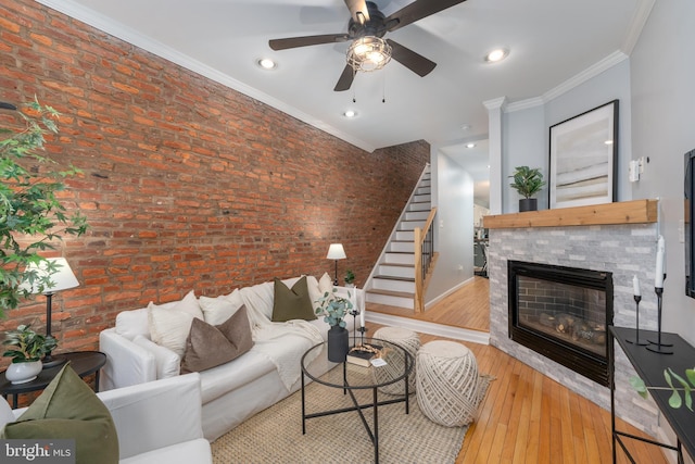 living room featuring ceiling fan, brick wall, a fireplace, crown molding, and light hardwood / wood-style flooring