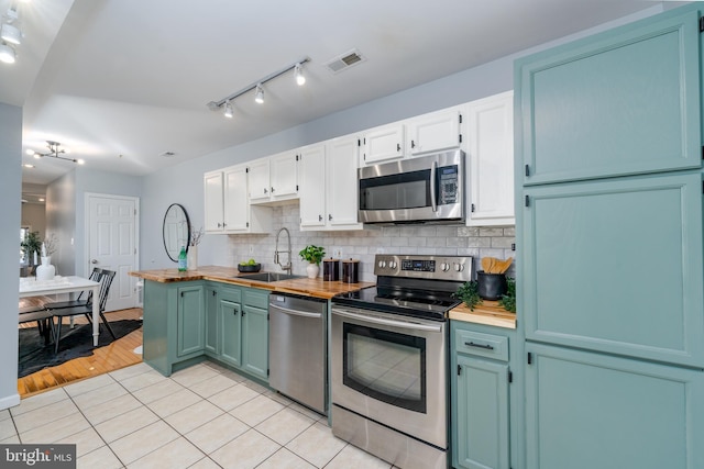 kitchen with light tile patterned floors, stainless steel appliances, tasteful backsplash, white cabinets, and sink