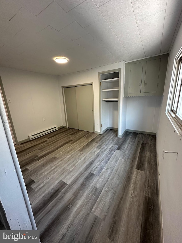 unfurnished bedroom with a baseboard heating unit, a closet, and dark hardwood / wood-style floors