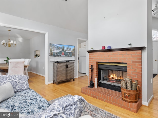 living room with a brick fireplace, light hardwood / wood-style floors, and an inviting chandelier