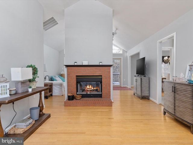 living room with vaulted ceiling, a brick fireplace, and light hardwood / wood-style flooring