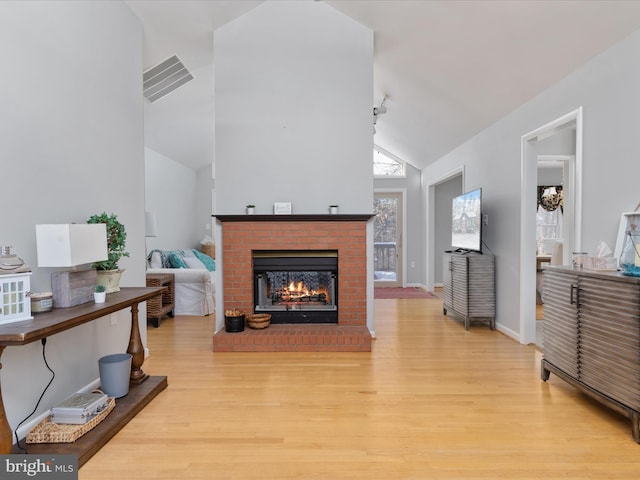 living room with a brick fireplace, vaulted ceiling, and light wood-type flooring