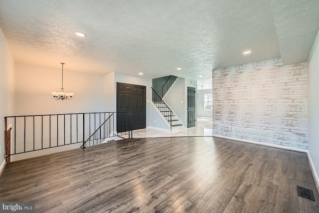 unfurnished room with hardwood / wood-style flooring, wooden walls, a textured ceiling, and a chandelier