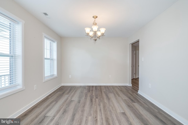 unfurnished room featuring a notable chandelier and light hardwood / wood-style flooring