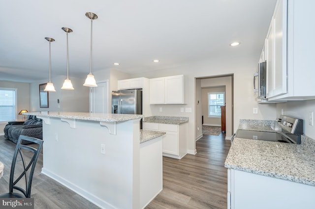 kitchen featuring white cabinets, appliances with stainless steel finishes, a center island, decorative light fixtures, and a kitchen breakfast bar