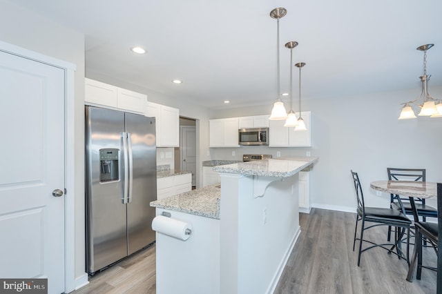 kitchen with appliances with stainless steel finishes, white cabinetry, hanging light fixtures, and a kitchen island