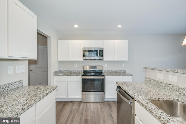 kitchen featuring light hardwood / wood-style floors, light stone countertops, white cabinetry, and appliances with stainless steel finishes