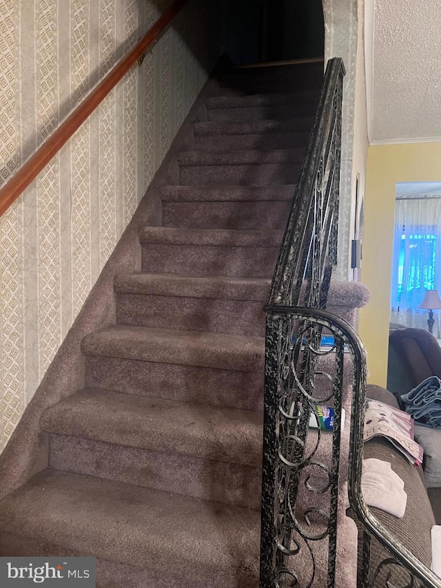 stairway with a textured ceiling and ornamental molding