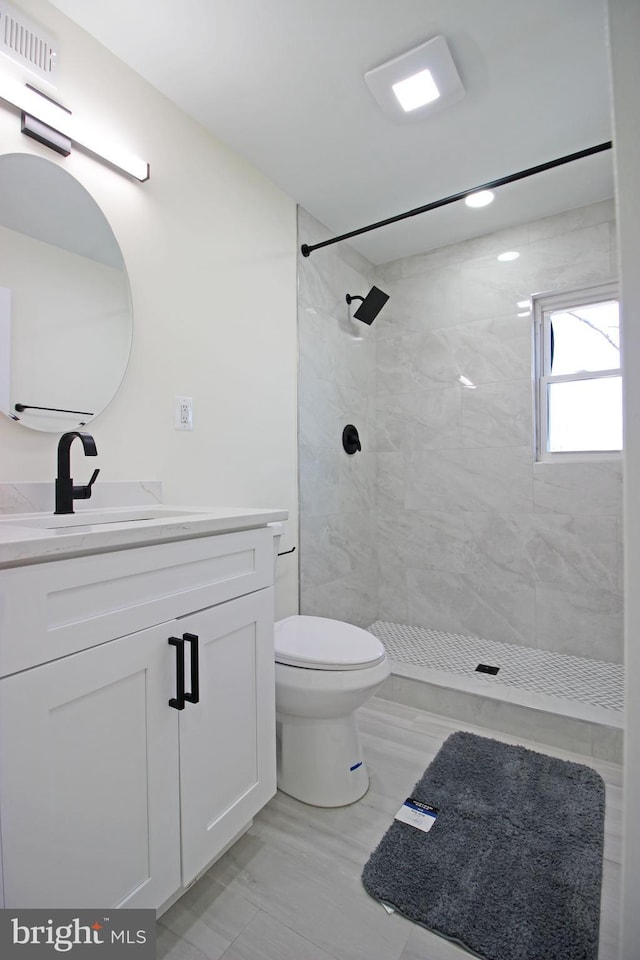 bathroom with toilet, vanity, and a tile shower