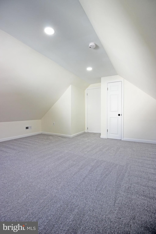 additional living space featuring vaulted ceiling and carpet flooring