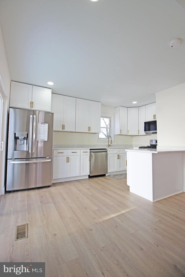 kitchen featuring light hardwood / wood-style floors, white cabinets, appliances with stainless steel finishes, and sink