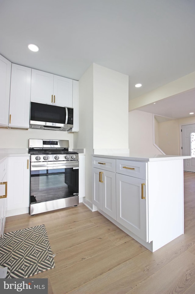 kitchen featuring light wood-type flooring, white cabinets, kitchen peninsula, and stainless steel appliances