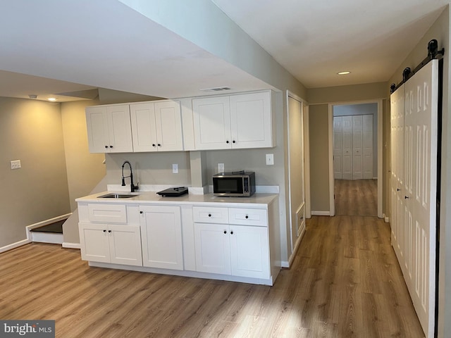 kitchen featuring white cabinets, sink, light hardwood / wood-style flooring, and a barn door