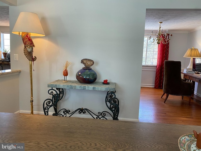 hall with crown molding, wood-type flooring, a wealth of natural light, and an inviting chandelier