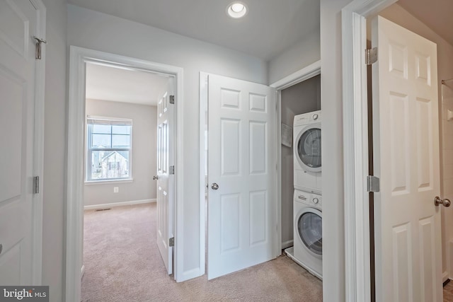 clothes washing area with light colored carpet and stacked washing maching and dryer