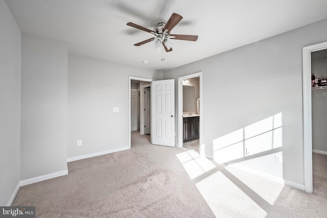 unfurnished bedroom featuring ensuite bath, a walk in closet, ceiling fan, and light carpet