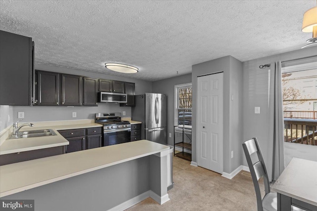 kitchen featuring a textured ceiling, appliances with stainless steel finishes, sink, kitchen peninsula, and light colored carpet