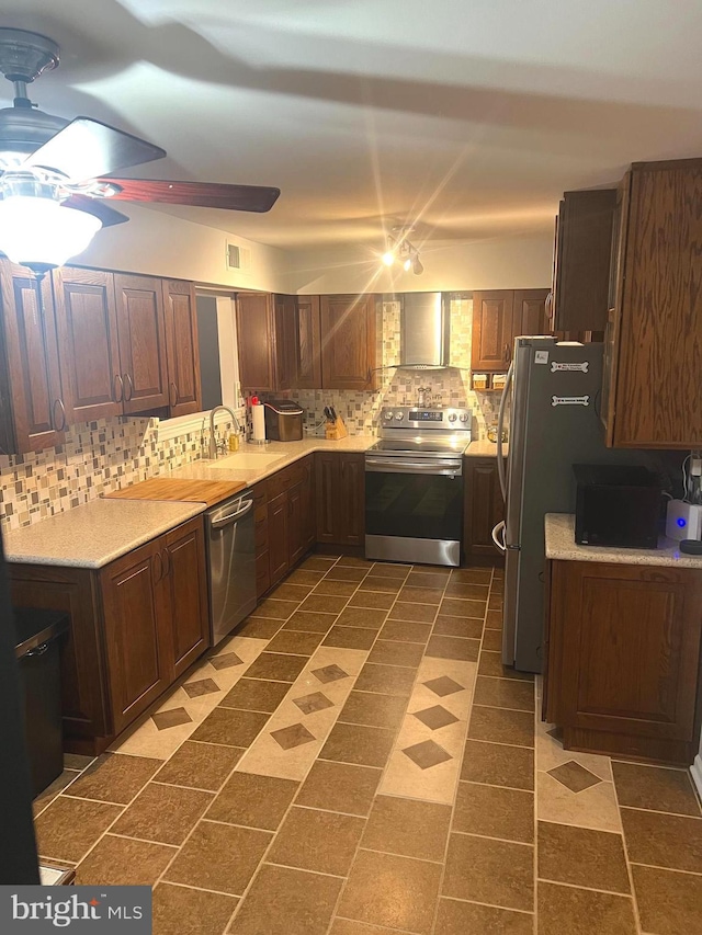 kitchen with ceiling fan, appliances with stainless steel finishes, decorative backsplash, wall chimney range hood, and sink