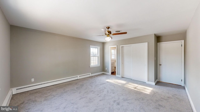 unfurnished bedroom featuring a baseboard heating unit, ceiling fan, two closets, and light carpet