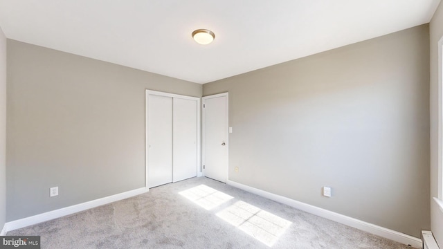 unfurnished bedroom with baseboard heating, light colored carpet, and a closet