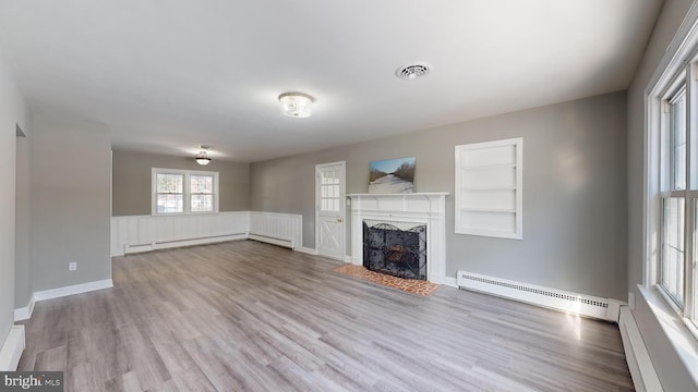 unfurnished living room with light wood-type flooring, built in shelves, baseboard heating, and a premium fireplace