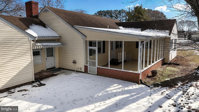 snow covered rear of property featuring a sunroom